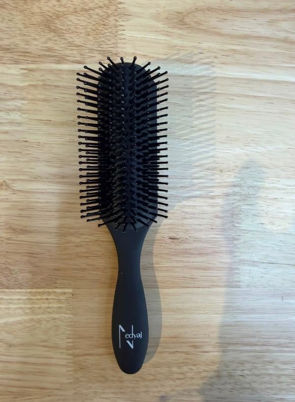 Avant : photo d'une brosse à cheveux noire Nedyaj posée sur une table en bois