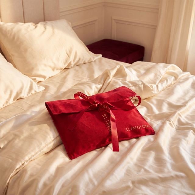 Pochette en satin rouge SLIMGLOSS posée sur un lit en satin crème